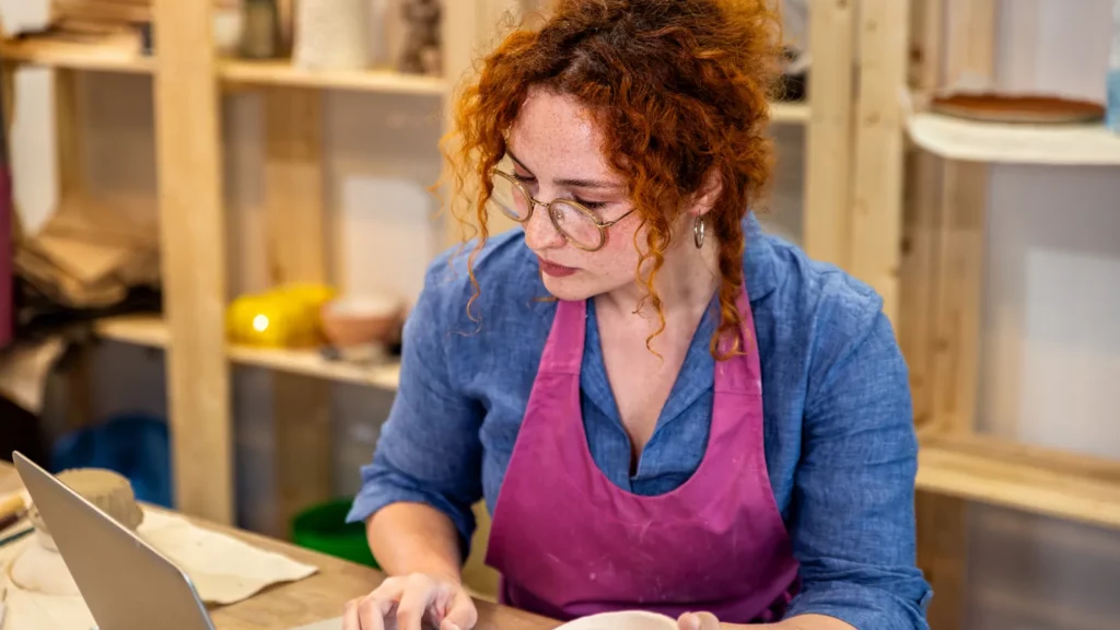 Artisane qui travaille sur son ordinateur portable dans son atelier de poterie